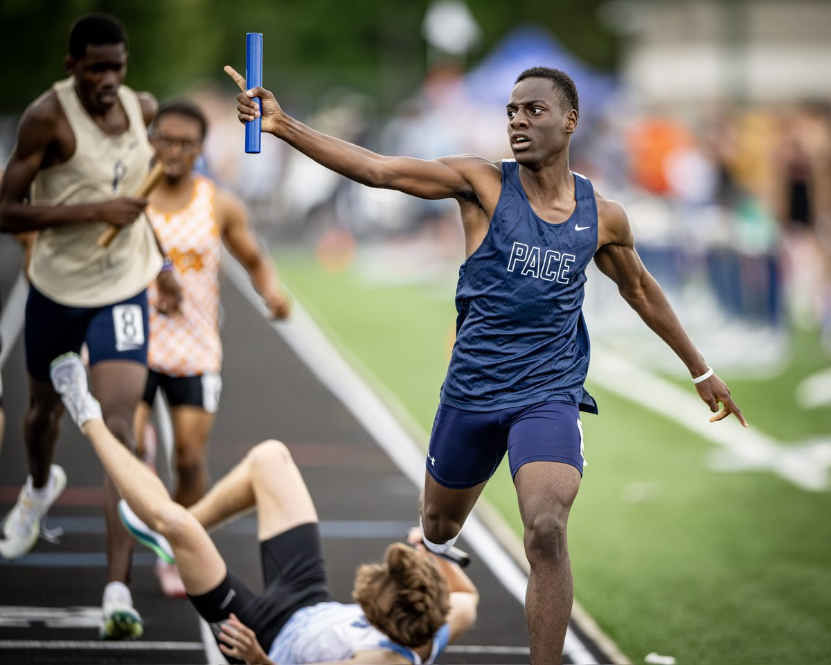 Zachary crossing the line with the baton raised as a competitor falls behind him